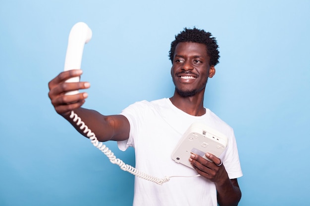 Uomo afroamericano che finge di fare selfie sul vecchio telefono fisso