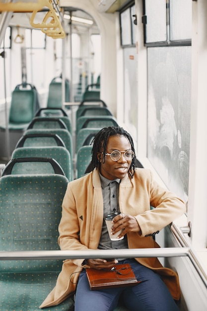 Uomo afroamericano che guida nel bus della città. ragazzo con un cappotto marrone. uomo con il caffè.