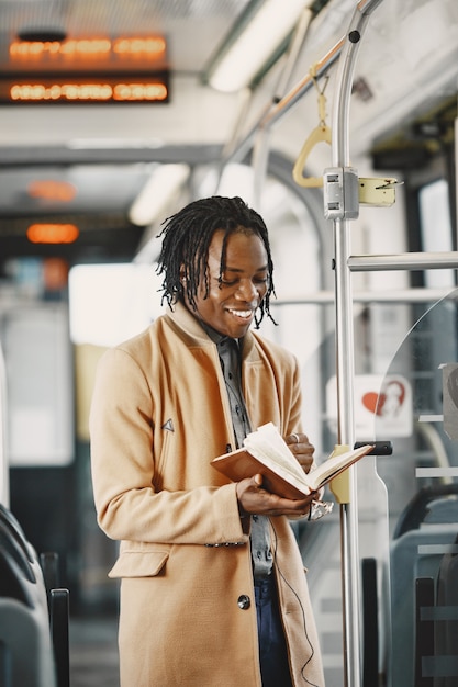 Афро-американский мужчина едет в городском автобусе. Парень в коричневом пальто. Человек с ноутбуком.