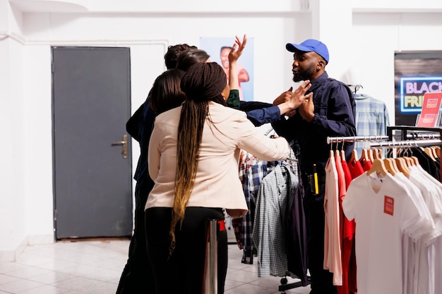 Free photo african american man, security officer talking and calming down black friday shoppers wait in line at clothing shop entrance. people shoppers arguing with clothes store staff, holiday shopping madness