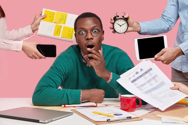 Free photo african american man sitting at desk surrounded with gadgets and papers