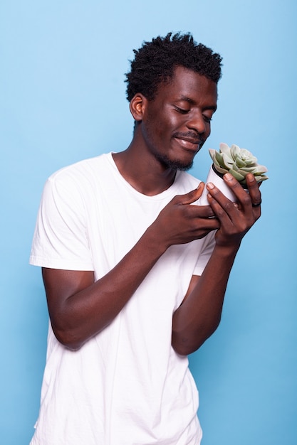 African american man smiling and looking at pot with plant