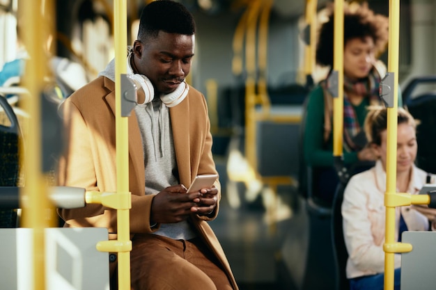 Foto gratuita sms uomo afroamericano sul telefono cellulare durante il pendolarismo con i mezzi pubblici