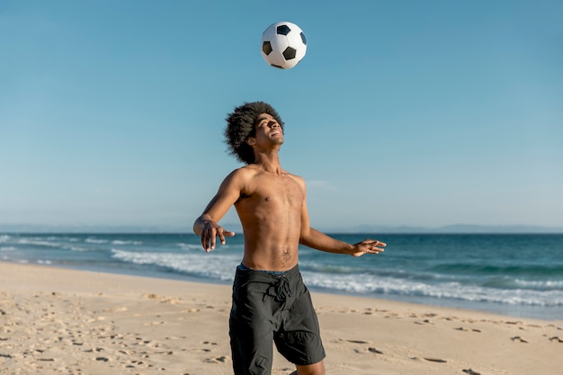 African American man tossing ball up on beach