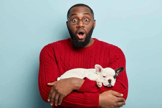 African American man wearing red sweater and holding little dog