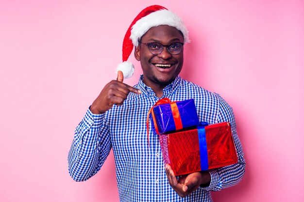 세련된 격자 무늬 셔츠를 입은 아프리카 계 미국인 남자는 분홍색 배경 studio.dark-skinned 산타 클로스 메리 크리스마스를 축하하는 선물 상자와 산타 모자에 큰 미소