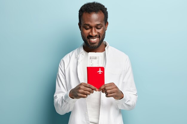 African American man wearing white shirt holding plane tickets