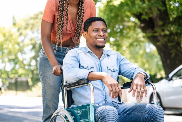 휠체어를 탄 아프리카계 미국인 남자가 여자친구와 야외에서 산책을 즐기고 있다