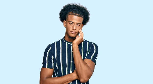 Афроамериканец с афро-волосами в повседневной одежде думает, что выглядит усталым и усталым от депрессии со скрещенными руками.