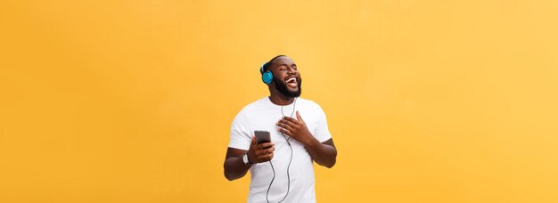 African american man with headphones listen and dance with music isolated on yellow background