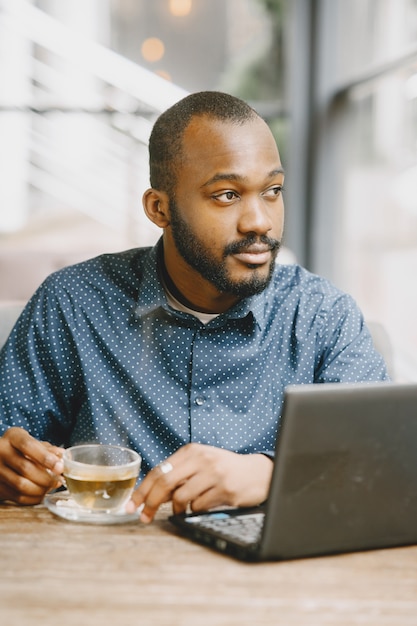 ノートパソコンの後ろで働くアフリカ系アメリカ人の男。カフェに座ってお茶を飲むあごひげを持つ男。
