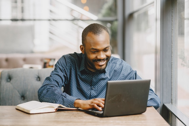 Uomo afroamericano che lavora dietro un computer portatile e scrive su un taccuino. uomo con la barba seduto in un caffè.