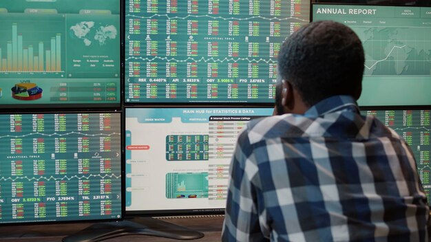 African american man working with forex market exchange on multi monitors workstation, analyzing stock funds and capital banking sales to buy and sell profit money. Financial growth.
