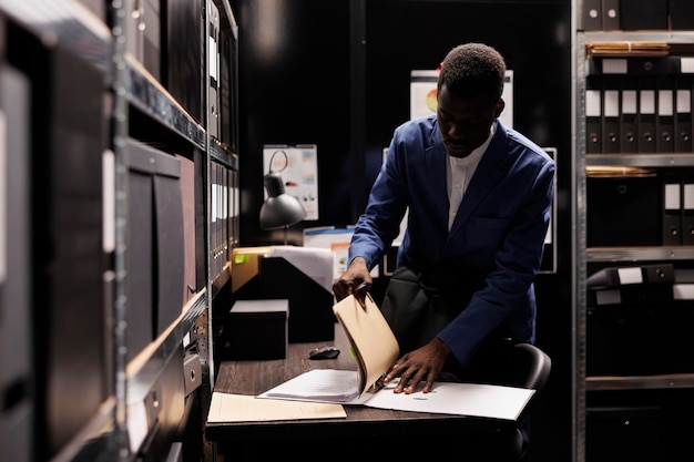 Free photo african american manager gathering his stuff, preparing to leave job late at night after working at accountancy report in file room. employee searching for bureaucracy record in corporate depository