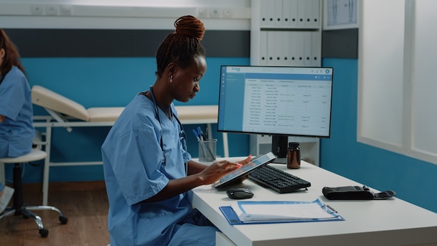 Афро-американская медсестра с помощью цифрового планшета для лечения
