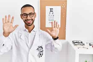 Free photo african american optician man standing by eyesight test showing and pointing up with fingers number ten while smiling confident and happy.