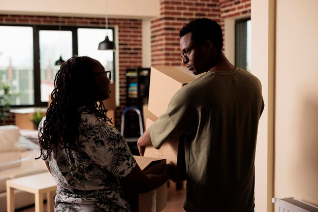 Афро-американские партнеры несут вещи, чтобы переехать в новую квартиру, используя коробки для украшения арендованного дома. Переезд в дом вместе, чтобы начать новые начинания в кредит.