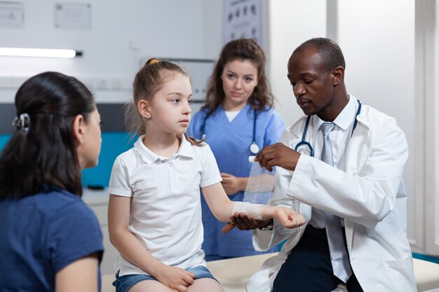 African american pediatrician doctor bandage broken bone of young child arm