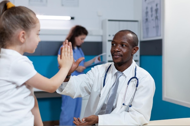 아프리카계 미국인 소아과 의사가 병원에서 진료를 받는 동안 어린 아이들에게 하이파이브를 줍니다. 의료 치료를 논의하는 질병 증상을 설명하는 치료사 남자