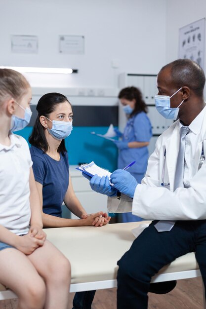 African american pediatrician doctor writing disease symptoms on clipboard