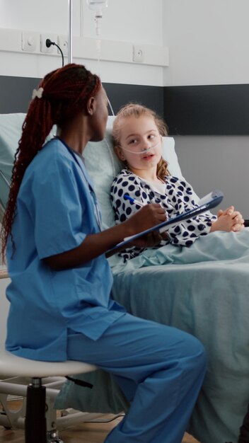African american pediatrician nurse discussing sickness symptoms with sick little child