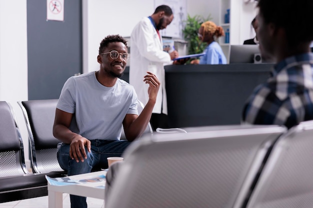 African american people talking about medicine and diagnosis in waiting room lobby at health center. Group of men sitting in area at hospital reception before attending checkup examination.