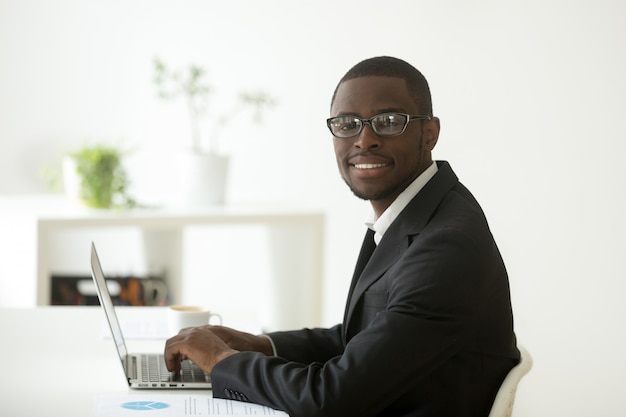 Бесплатное фото Афро-американский улыбающийся бизнесмен в костюме и очках, глядя на камеру