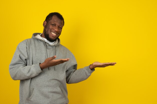 African-American smiling man who opened his hands , standing in front of the yellow wall. 