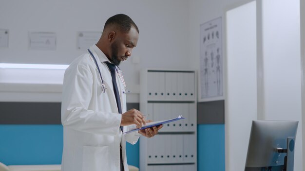 アフリカ系アメリカ人の専門医が、病院のオフィスで医療治療に従事しているときに、コンピューターで医療の専門知識を分析する病気のレポート文書をチェックしています。医療サービス