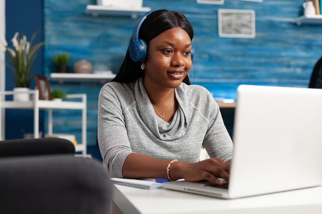 African american student wearing headphones browsing information composing blog article