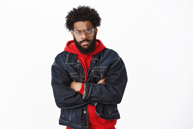 african-american stylish bearded man with glasses and pierced nose frowning crossing arms on chest in insulted pose, being gloomy as friend tricked him.