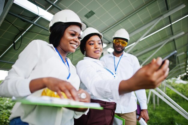 African american technician checks the maintenance of the solar panels Group of three black engineers meeting at solar station Make selfie by phone