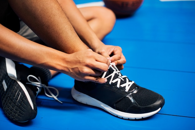 Free photo african american teenage boy tying his shoe laces on a basketball court