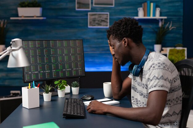 African american trader looking at stock market analyzing crypto currency growth on computer working remote from home. Young entrepreneur checking data charts monitoring global investment numbers