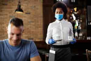 Free photo african american waitress serving coffee while wearing face mask and gloves