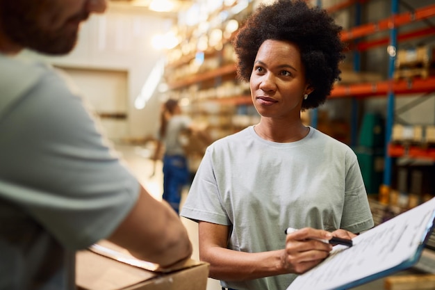 Free photo african american warehouse worker going through check list while communicating with her colleague in distribution warehouse