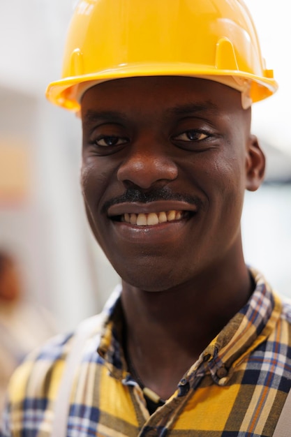 安全ヘルメットをかぶったアフリカ系アメリカ人の倉庫労働者の顔のポートレート。カメラを間近で見て産業用保護具で幸せな表情をした笑顔の倉庫ローダー