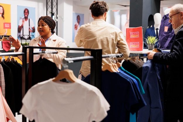 Foto gratuita assistente di un negozio di abbigliamento di donna afroamericana che fa gesti con le mani chiedendo agli acquirenti di rallentare e rimanere calmi durante lo shopping del black friday nel negozio di abiti. vende stagionali al dettaglio