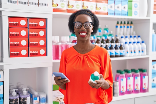 Афро-американская клиентка с помощью смартфона держит бутылку с лекарством в аптеке