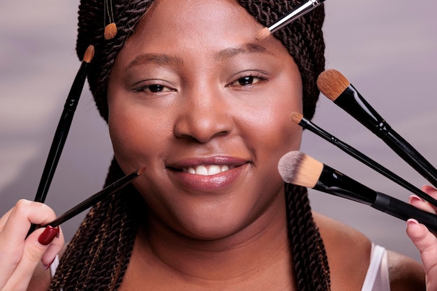 Free photo african american woman getting professional make up portrait. makeup artists hands applying eye shadows and powder on model face, using decorative cosmetics brushes close up