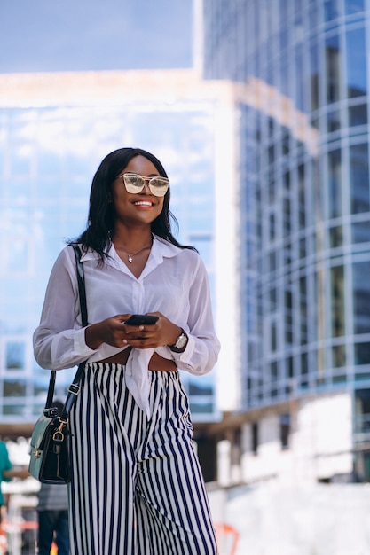 Donna afroamericana all'aperto dal grattacielo con il telefono