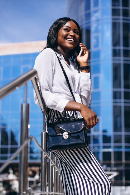 African american woman outdoors by the skyscraper with phone