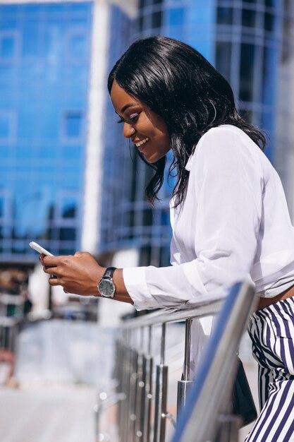 African american woman outdoors by the skyscraper with phone