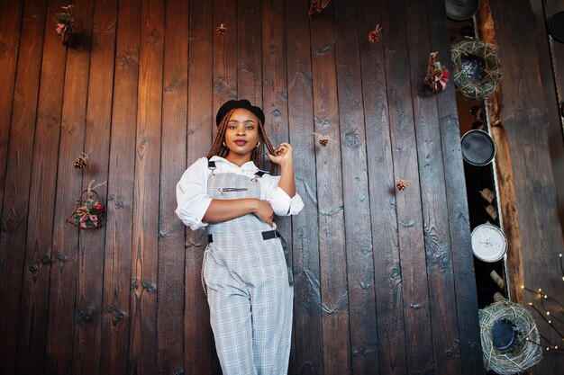 African american woman in overalls and beret against wooden wall