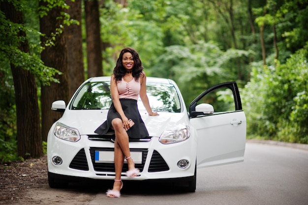 숲길에서 흰색 차에 맞서 포즈를 취한 아프리카계 미국인 여성