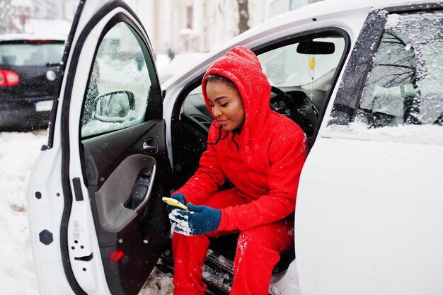 携帯電話で冬の雪の日に車の中に座っている赤いパーカーのアフリカ系アメリカ人女性