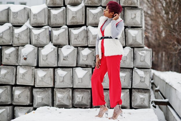 겨울날 눈 덮인 돌 배경에 포즈를 취한 빨간 바지와 흰색 모피 코트 재킷을 입은 아프리카계 미국인 여성