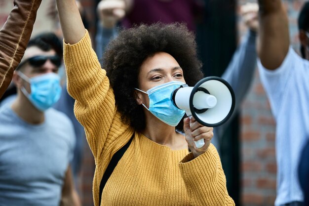 african american woman shouting through megaphone while wearing protective face mask on a antiracism protest