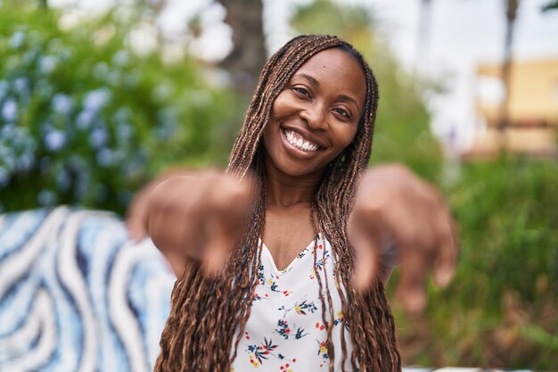 公園でカメラを指で指して自信を持って笑顔のアフリカ系アメリカ人女性