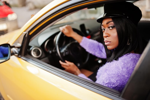 African american woman at violet dress and cap posed at yellow car